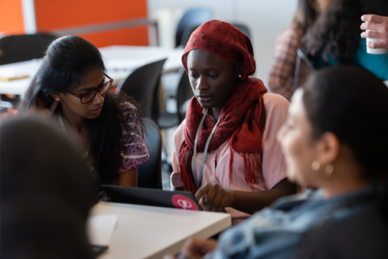 Three girls sitting around a computer in a classroom. 