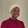 A young black woman in a beige, hair wrap and plum-colored blouse